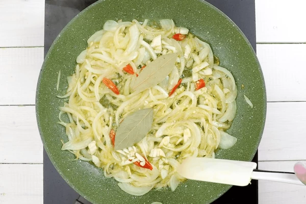 На хорошо разогретой с оливковым маслом сковороде обжарить лук до золотистого цвета, добавить чеснок, перец и лавровый лист, перемешать.