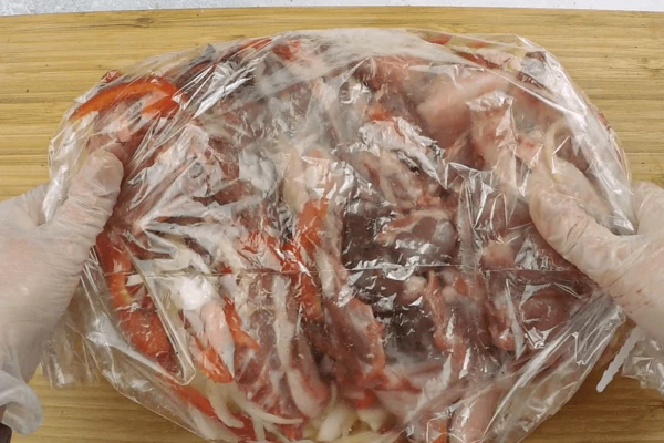 Овощи переложить в смазанный растительным маслом рукав, затем добавить разделанное на порции мясо, закрыть рукав с другой стороны клипсой.