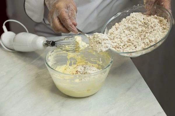 Смешайте отдельно муку, разрыхлитель и овсяные хлопья. Добавляйте порциями в масло, продолжая взбивать тесто.