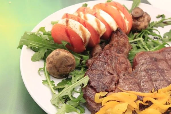 На тарелку с одной стороны выложить салат рукколу, помидоры и сыр моцареллу, нарезанные кружочками толщиной 1-1,5см. Сбрызнуть оливковым маслом и соевым топингом. Рядом положить грибы - гриль. С другой стороны выложить обжаренный стейк, украсить нарезанным перцем -гриль.