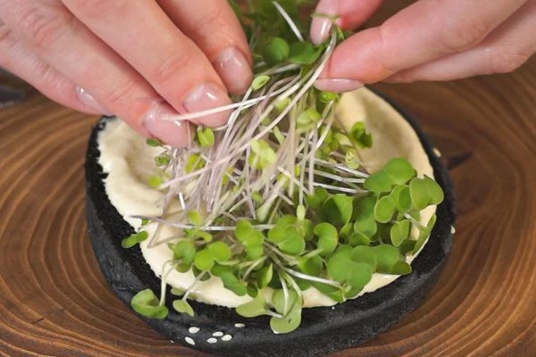 На нижнюю часть булочки намазать соус Цезарь, выложить микрозелень. Микрозелень можно заменить листьями салата. 