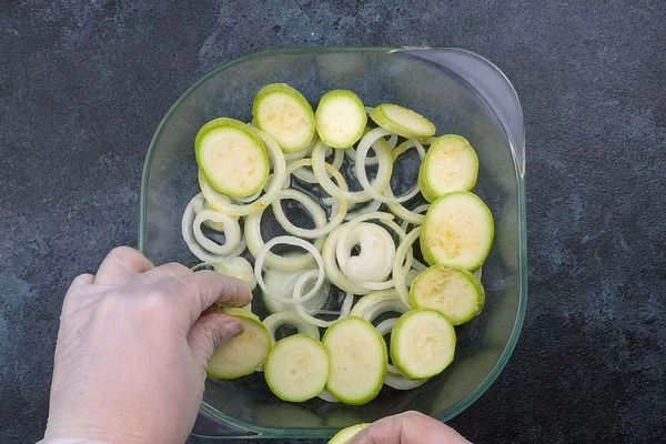  На дно смазанной формы выложить лук, кабачки и помидоры.