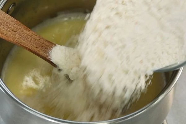 Смешать воду с молоком. Всыпать соль и сахар, добавить сливочное масло. Довести до кипения и снять с огня. Добавить всю муку и интенсивно помешивать деревянной лопаткой. Вернуть на плиту на средний огонь, помешивать пока на дне сотейника не появится бархатная пленка (примерно 2-3 минуты).