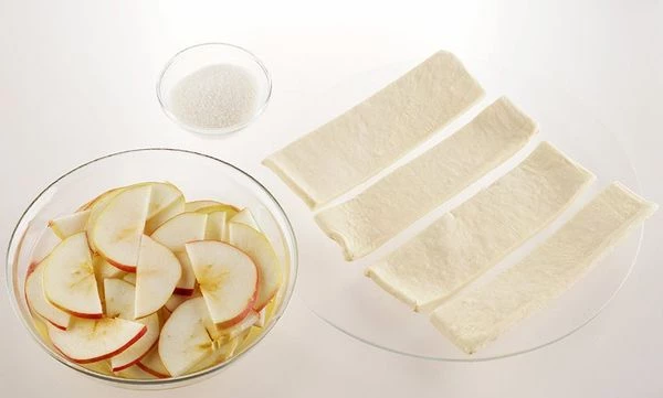 Тесто разморозить, нарезать полосками, шириной примерно 3-4 см. Яблоки промыть, нарезать тонкими полукольцами, залить водой и поставить в микроволновую печь на 1-2 минуты ( в зависимости от мощности Вашего оборудования), чтобы они были немного мягкими и не ломались в процессе приготовления.