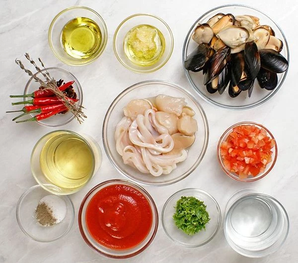 Разморозить мидии (если варено-мороженые) естественным способом на нижней полке холодильника. Промыть под проточной холодной водой, зачистить ракушки, удалить волосатый мускул, убрать сломанные ракушки. Кальмары и гребешки разморозить, нарезать колечками. Помидоры разрезать пополам, удалить семена, нарезать небольшим кубиком.