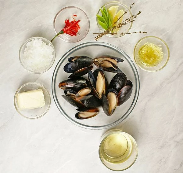 Лук нарезать мелкой крошкой. Мидии разморозить (если варено-мороженые), промыть, перебрать от ломанных ракушек. Чеснок натереть и смешать с оливковым маслом. Перец чили нарезать тонкой соломкой.