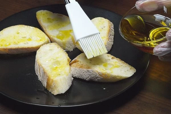 Багет нарезать на порции, под углом, толщиной примерно 1-1,5 см. Смазать оливковым маслом.