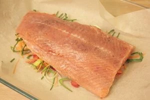 В центр бумаги для запекания (размер пергамента должен быть больше филе,чтобы можно было завернуть внахлест) выложить 1/2 часть сливочного масла, затем смесь из нарезанных овощей. На овощи - филе подготовленной рыбы.