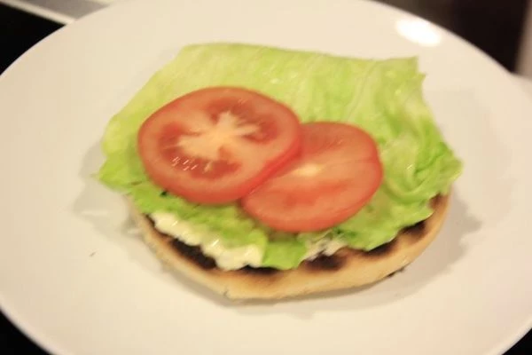 Помидор нарезать кружочками, толщиной 1-1,5см. Лук репчатый нарезать тонкими колечками и замариновать в лимонном соке. Выложить на подогретую булочку : соус, лист салата, помидор.