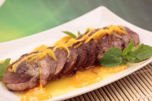 На тарелку налить немного соуса, утиную грудку нарезать тонкими пластиками, выложить на соус, сверху украсить цедрой и дольками мандарина.