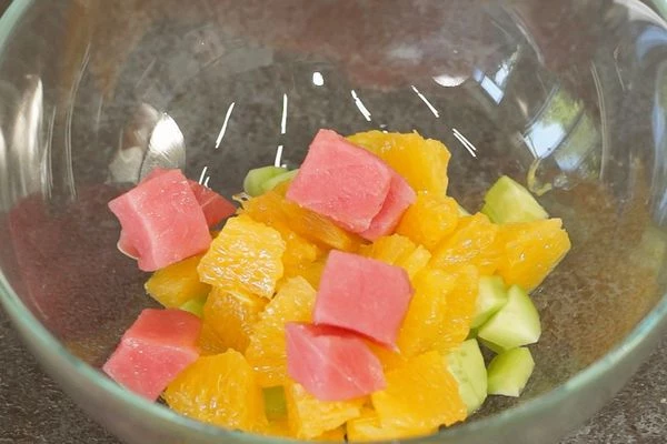 Тунец разморозить на нижней полке холодильника, обсушить на салфетке, нарезать кубиком 0,7 на 0,7 см. 
Огурцы очистить от кожуры, нарезать кубиком 0,7 на 0,7 см. 
Один апельсин очистить от кожуры, вырезать сегменты из мякоти (без пленок и косточек). Сегменты порезать на 2 части. 
Смешать нарезанный тунец, огурцы и сегменты апельсина.
