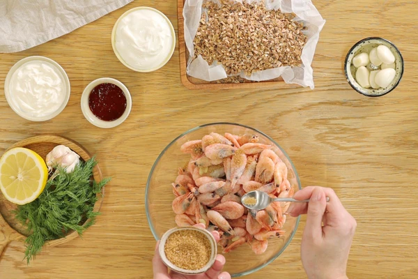 Креветки разморозить на нижней полке холодильника. Лимон вымыть, разрезать пополам, выдавить сок из половинки. Чеснок очистить, мелко нарезать.
Выложить креветки в глубокую емкость и добавить к ним оливковое масло, сок лимона, измельченный чеснок, соль и сахарный песок. Все тщательно перемешать и поставить в холодильник на 60 минут для маринования.
