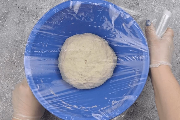 Накрыть пищевой пленкой, дать подняться около часа в теплом месте. Затем тесто обмять, хорошо выпуская пузырьки с воздухом, накрыть пленкой и дать подняться еще около 20 минут.