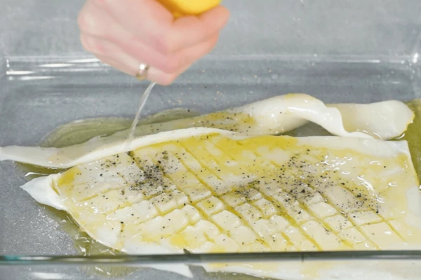 Подготовленную каракатицу переложить в емкость, залить оливковым маслом, сбрызнуть соком лимона, посолить и поперчить. Оставить мариноваться на 15 минут.
