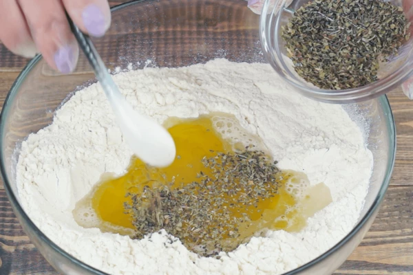 В глубокой чашке смешать муку, воду, масло и сушеные травы. 