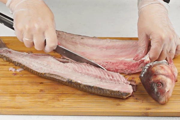 Далее удалить голову,  разрезать вдоль хребта на два филе с кожей, очистить от чешуи (если есть необходимость).