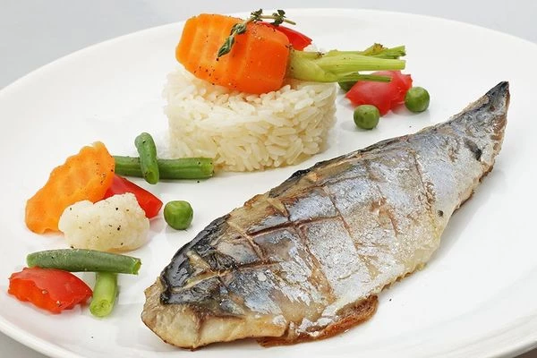 На тарелку, с помощью кулинарного кольца, выложить башенкой рис, затем украсить бланшированными овощами. Рядом выложить филе скумбрии.