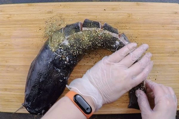 По всей тушке сделать надрезы с шагом 4-5 см. Натереть сома специями.