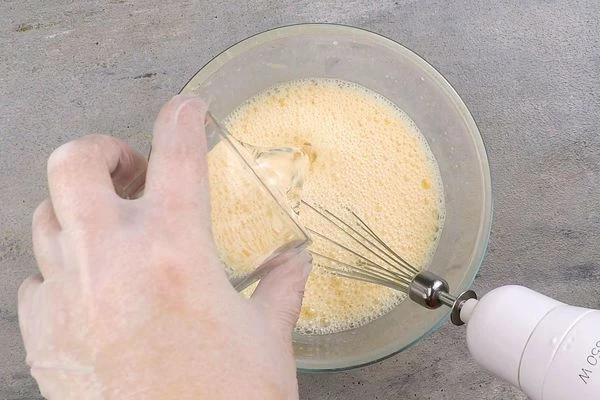 Сливочное масло растопить. В глубокой чашке смешать молоко, яйца, сахар, соль, разрыхлитель, воду. 