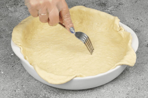 Готовое тесто разделить на две части, первую раскатать в пласт и выложить в смазанную форму, оставляя небольшой край, сделать по дну наколы вилкой. У нас форма 24 см, высота 5 см.