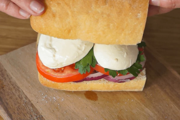 Помидоры нарезать кружочками, лук кольцом, шарик моцареллы разрезать на 2-3 части.
Чиабатту разрезать на две части, затем каждую еще по вдоль. Одну половинку сбрызнуть оливковым маслом, посолить, поперчить, выложить лук, сверху помидоры, листики зелени, пластики сыра, накрыть второй половиной.