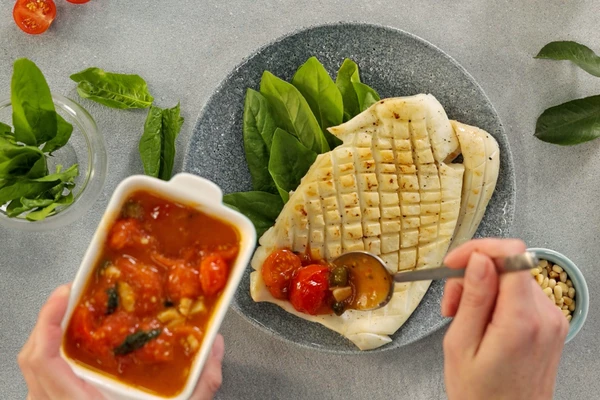 На тарелку для подачи выложить листья шпината, на них каракатицу. Оформить соусом из томатов черри. 