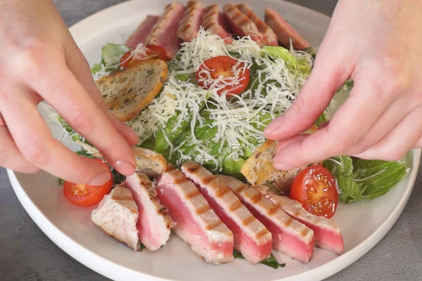 На тарелку выложить заправленные листья салата, нарезанные ломтики тунца, томаты черри, посыпать тертым пармезаном. Оформить крутонами.  Приятного аппетита!

