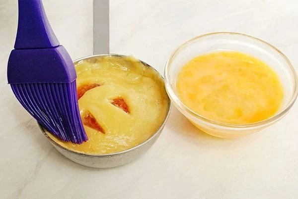 Закрыть начинку  кружками с рожицей, приклеив на яичную смесь. Смазать печенье сверху яйцом.