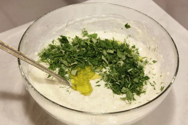 Добавить к сыру муку, соль, специи, хорошо перемешать, влить йогурт, добавить яйца, разрыхлитель, зелень, оливковое масло и нарезанные оливки.