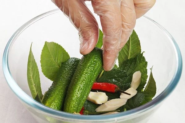 В глубокую чашку выложить на дно листья смородины, вишни, зубчики чеснока, перец чили и нарезанный кусочками корень хрена. Сверху плотно уложить огурчики.