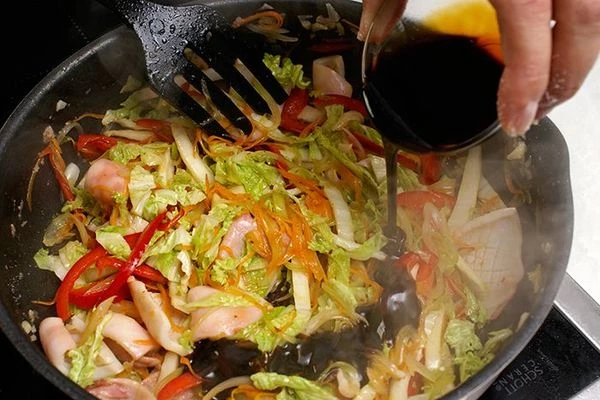 Добавить красный перец соломкой, обжарить 2-3 минуты. В конце приготовления добавить китайскую капусту, обжаренный кальмар и влить соус терияки. Перемешивать 1-2 минуты, снять с огня.