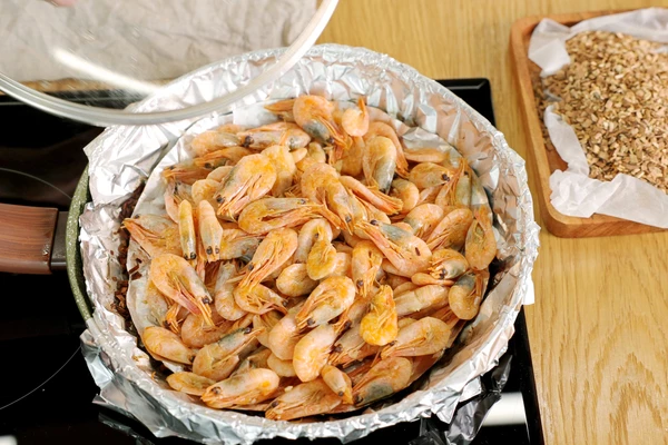 На фольгу разложить креветки и закрыть плотно крышкой.
Установить средний огонь, готовить 15 минут.
По истечению времени выключить огонь и дайте деликатесу полностью насытиться дымом. Когда емкость остынет — подавать копченость на стол.
