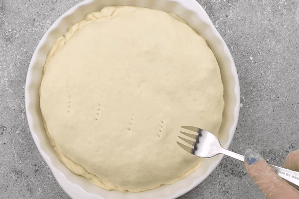 Накрыть пирог вторым пластом теста, защипать края внутрь. Сделать проколы вилкой сверху. 