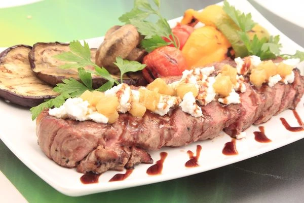 Мясо нарежьте пластиками, выложите на тарелку, украсьте сыром рикота и чатни из груши. Рядом положите овощи-гриль, зелень, полейте соевым топингом.