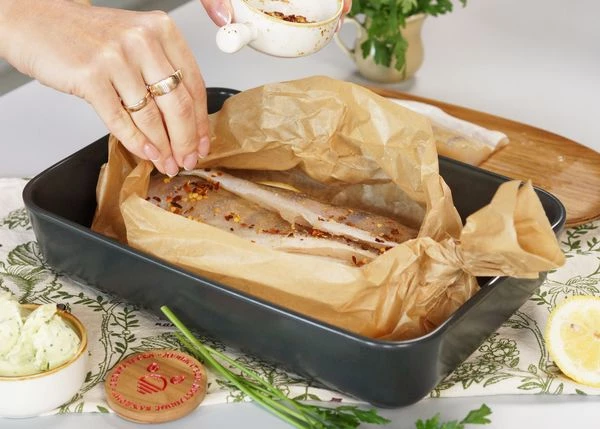 На каждое филе выложить по кусочку сливочного масла. Посыпать измельченным перцем чили. Завернуть пергамент. Готовить в разогретой до 180 градусов духовке в течение 7-10 минут. 