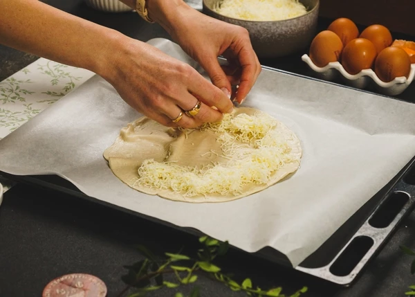 Лепешку Роти немного разморозить. Выложить на пергамент. По краю выложить натертый сыр.