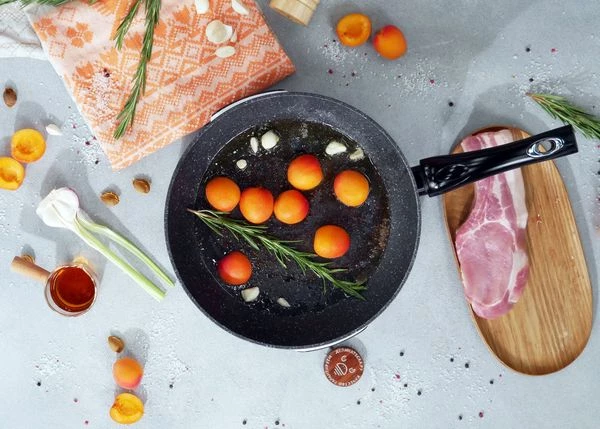 В эту же сковороду выложить половинки абрикосов, зубчик чеснока и веточку розмарина. Обжаривать в течение минуты.