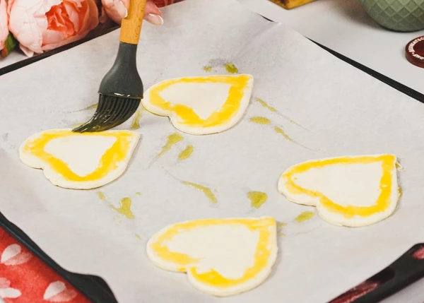 Нижнее сердечко переложить на противень с пергаментом, смазанный маслом. Края смазать взбитым желтком.