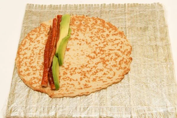 Угря для суши и авокадо нарежьте тонкими длинными ломтиками и выложите на блинчик