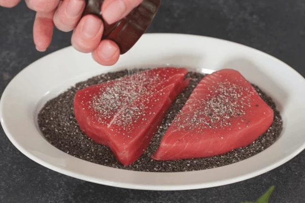 Тунец разморозить на нижней полке холодильника, обсушить на салфетке. На плоскую тарелку высыпать семена чиа, выложить тунца,  посолить и поперчить, запанировать в нем тунца.

