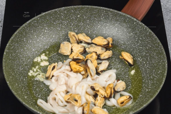 На разогретую с растительным маслом сковороду добавить мелко нарезанный чеснок, затем морепродукты, обжарить 2-3 минуты, дольше не надо, иначе станут резиновыми, посолить, поперчить по вкусу. 