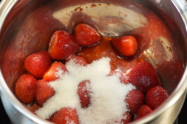 Клубнику разморозить, переложить в сотейник, добавить сахар и ванилин, довести до кипения. Затем снизить нагрев и томить 5 - 7 минут на среднем огне. 
