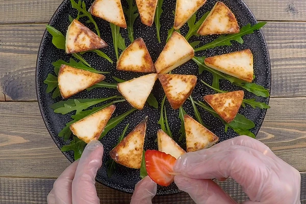 Клубнику наколоть на шпажки или зубочистки, украсить сыр сверху.