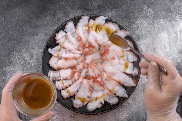 Пластики осьминога выложить в один слой на тарелку. Сбрызнуть заправкой, оставить подмариноваться 30-40 минут.