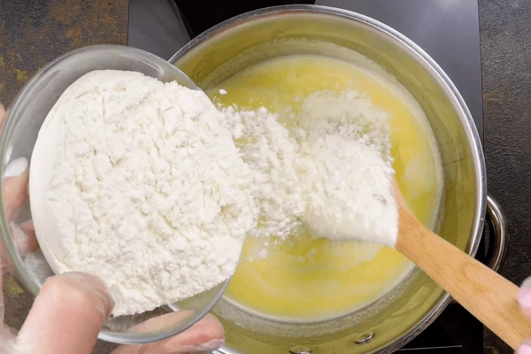 Снять кастрюлю с огня, всыпать муку и, интенсивно размешивая, заварить ее в молочно-масляной жидкости. Тесто должно получиться гладким, без комков. 