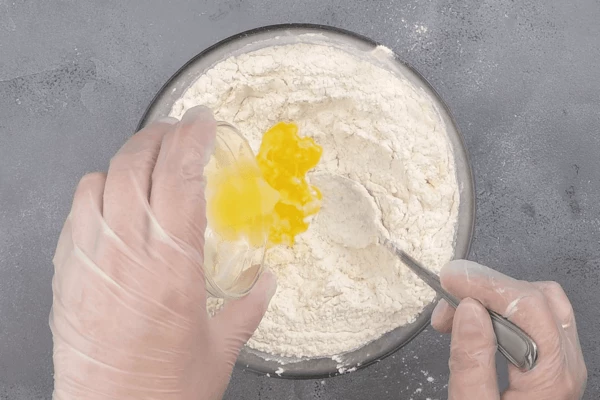 В центре сделать углубление, добавить туда соль, сахар, яйцо, растопленное сливочное масло. Перемешать, влить молоко и замесить тесто. 