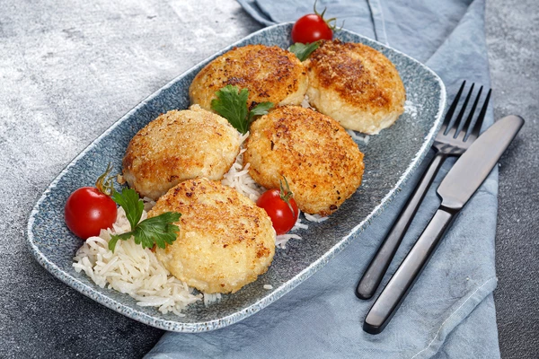 На гарнир к котлетам из пикши подать отварной рис, украсить зеленью и помидорами черри.