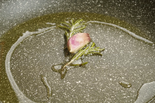 На разогретую с растительным маслом сковороду выложить раздавленный чеснок и веточку розмарина, немного прогреть.