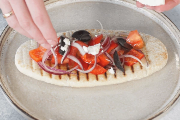 На тарелку для подачи выложить питу, на нее выложить салат, посыпать кусочками феты.