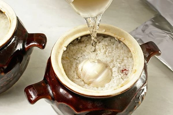 Добавить головку чеснока и залить водой, чтобы закрыть рис примерное на 1,5см